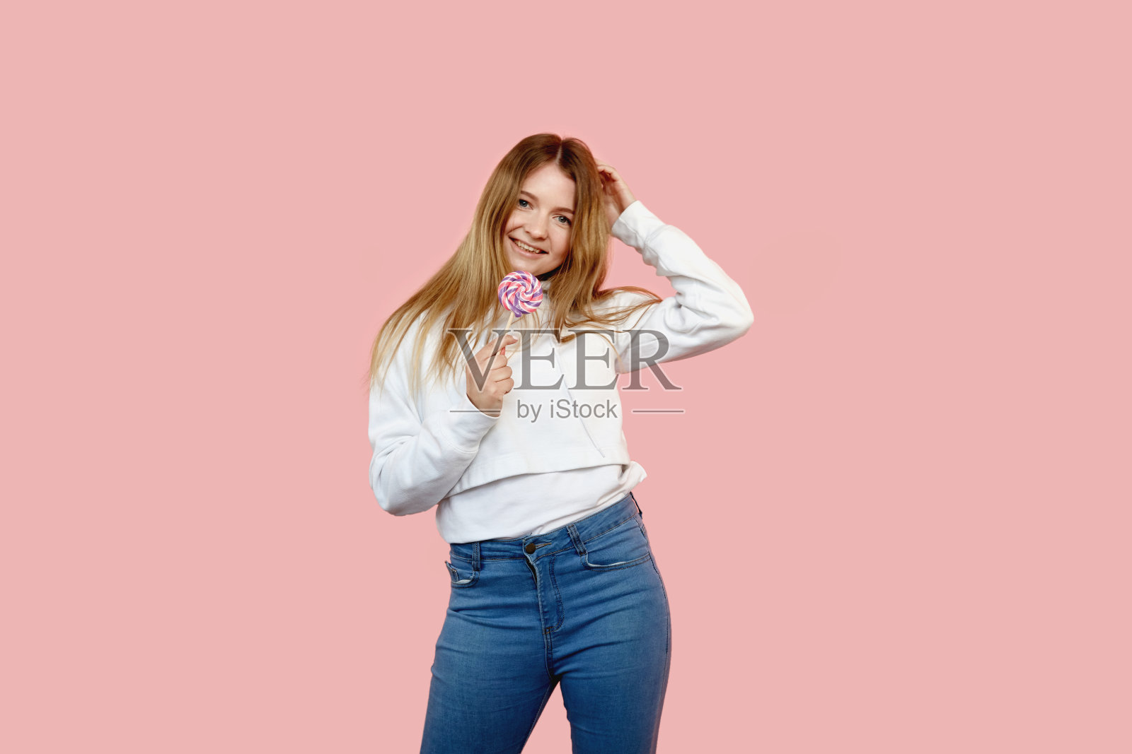 一个漂亮的年轻女孩，手里拿着一根彩色的棒棒糖。照片摄影图片