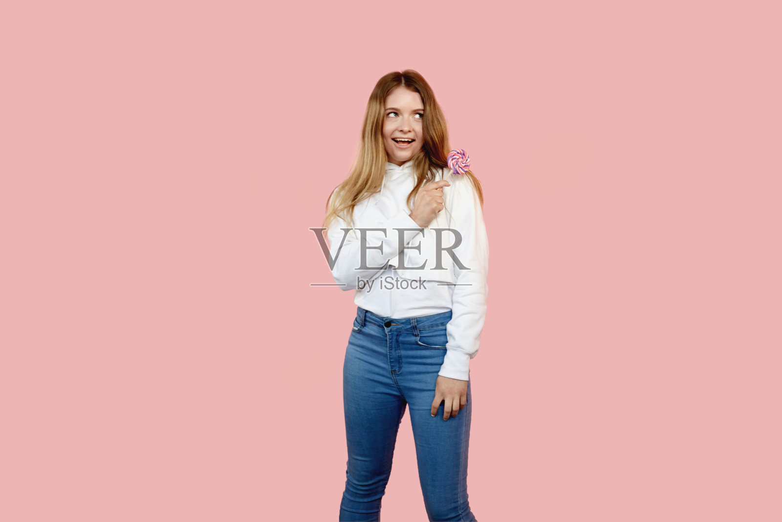 微笑的女孩手里拿着一根甜蜜的棒棒糖，看向一边。照片摄影图片