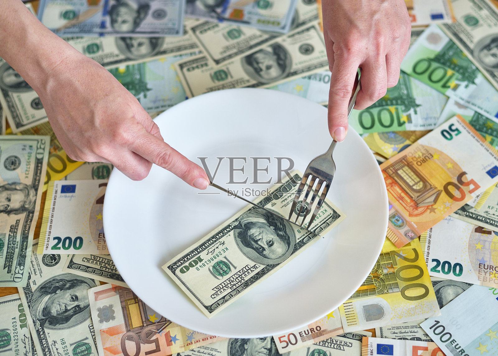 美钞躺在盘子里。拿着叉子的手伸向美元照片摄影图片