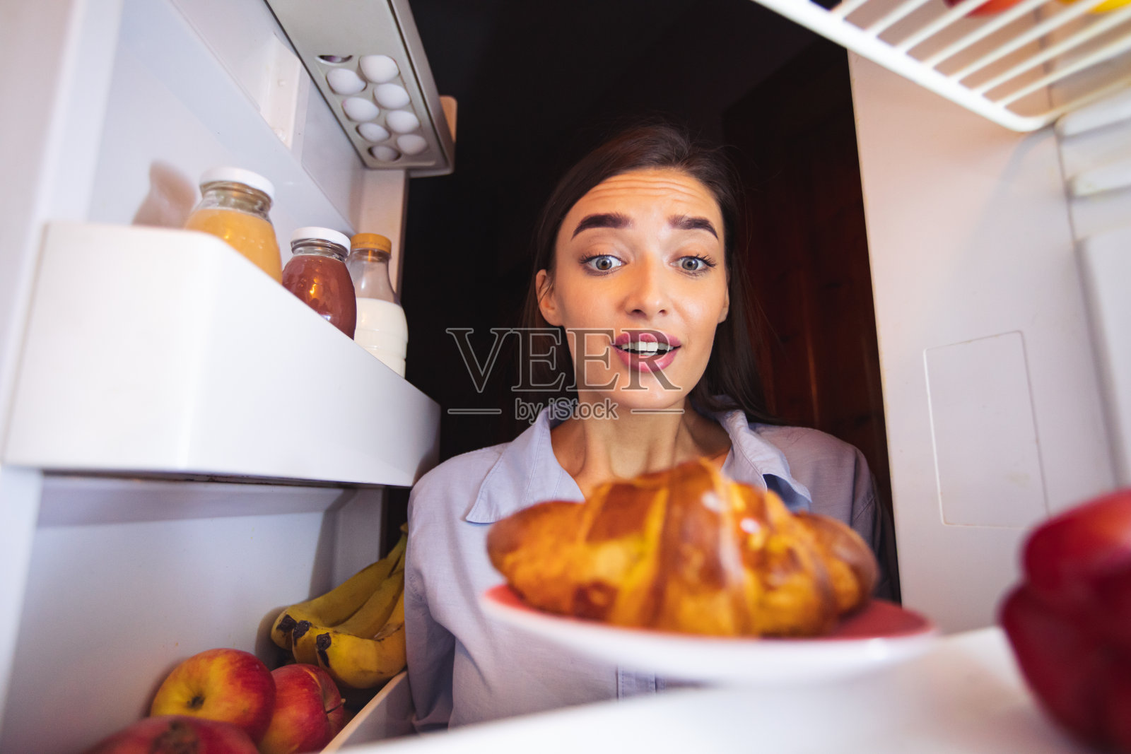 饥饿的女孩看着冰箱里的新鲜羊角面包照片摄影图片