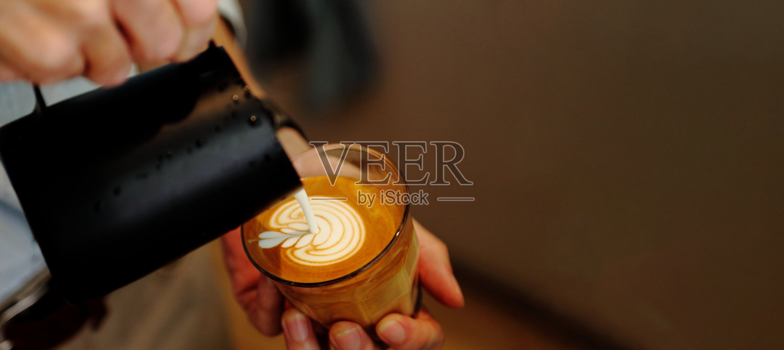 咖啡师用大壶将牛奶泡沫倒进顶部有郁金香图案的拿铁咖啡中照片摄影图片