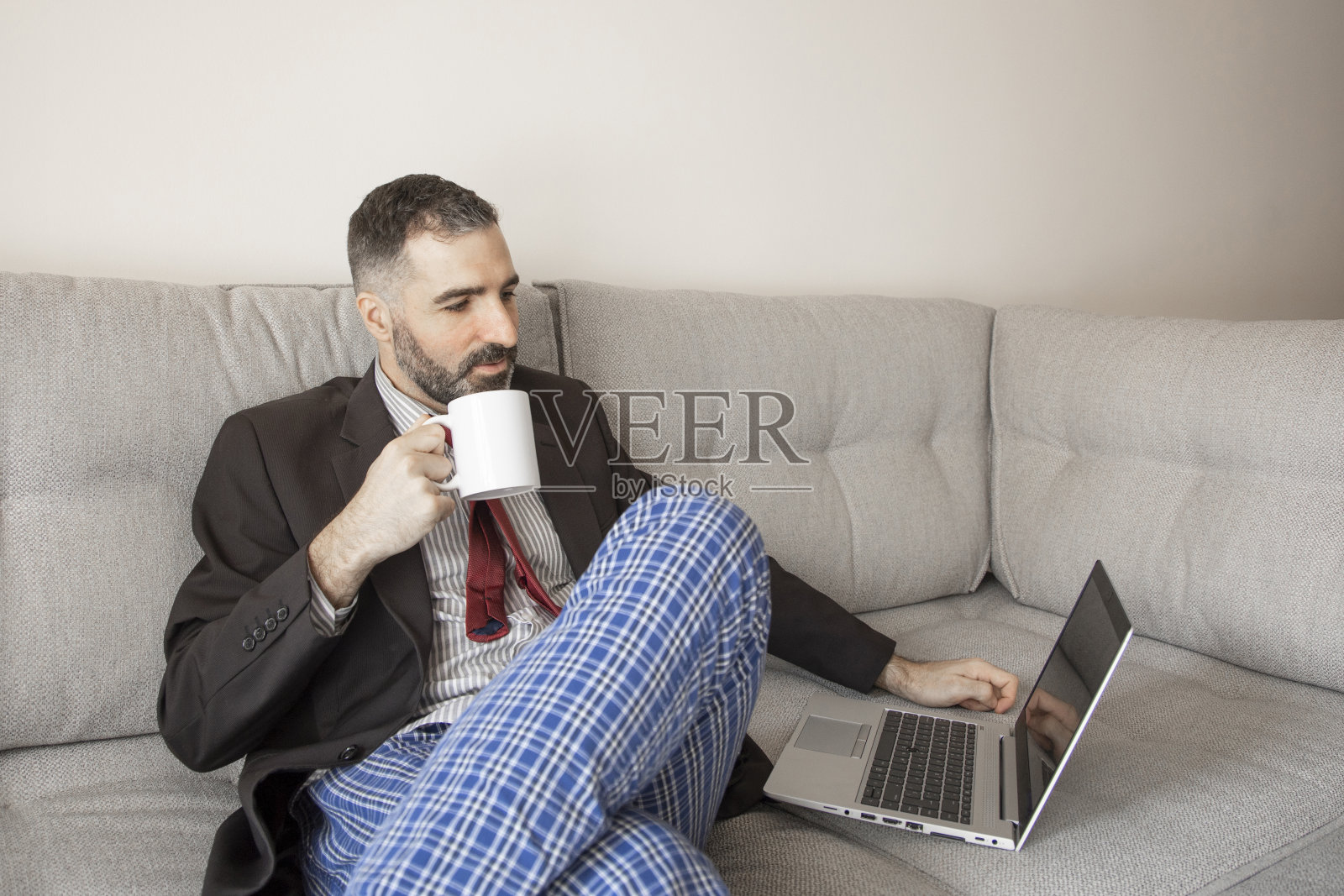穿着西装和睡裤在家工作喝着咖啡的商人照片摄影图片
