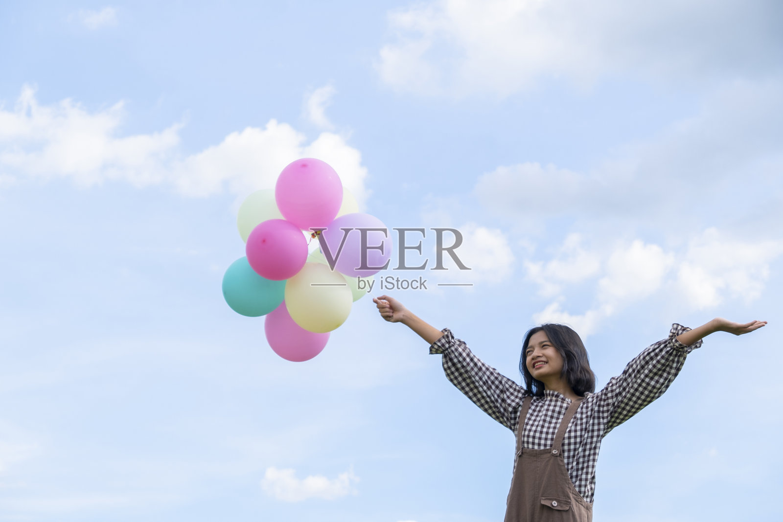 快乐的年轻亚洲女孩拿着五颜六色的气球与蓝天的背景。照片摄影图片