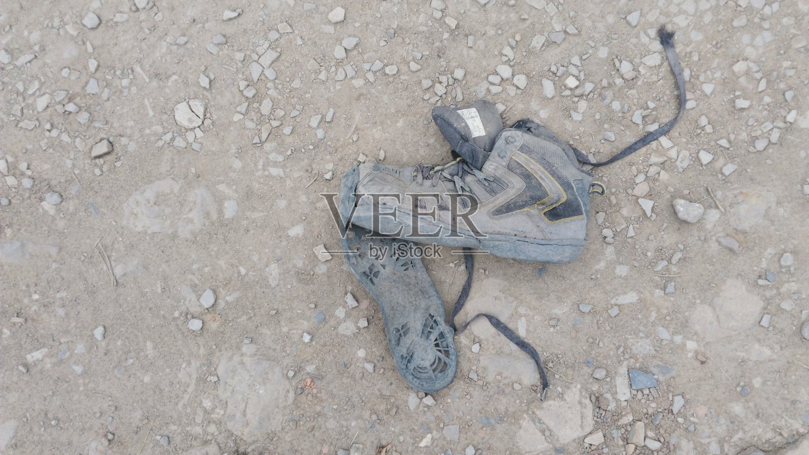 被一个无家可归的行人丢弃在泥土路上的破损鞋子照片摄影图片