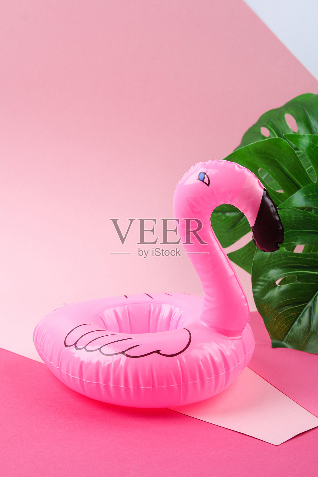 充气粉红色迷你火烈鸟和热带叶怪兽在粉红色的背景。创意的夏季海滩概念。火烈鸟趋势充气玩具。照片摄影图片