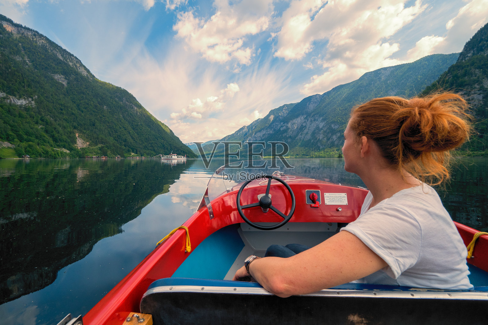 在奥地利萨尔兹卡默古特地区哈尔斯塔特附近的迷人山景前，女游客乘坐着小红船在哈尔斯塔特湖上巡航，OÖ照片摄影图片