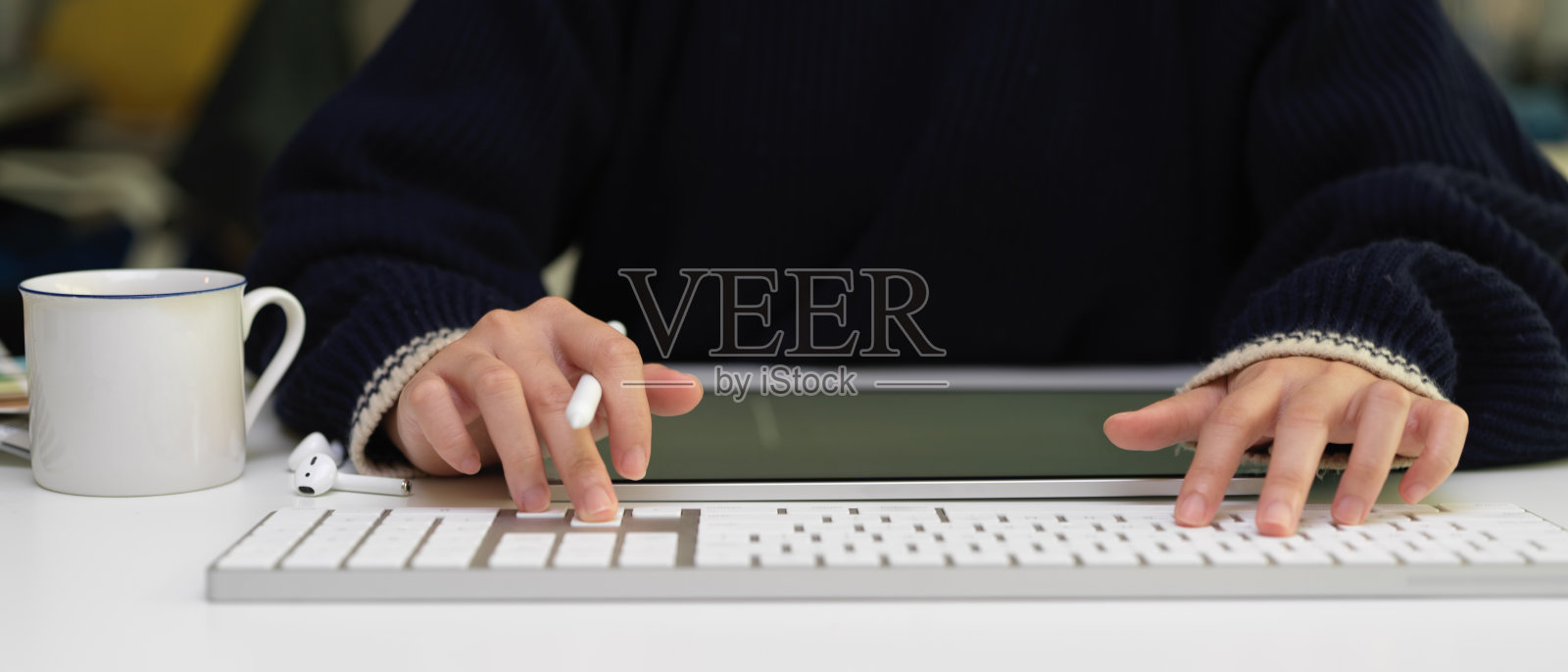 女员工在白色办公桌上用电脑键盘打字，无线耳机，数字平板电脑和办公用品照片摄影图片