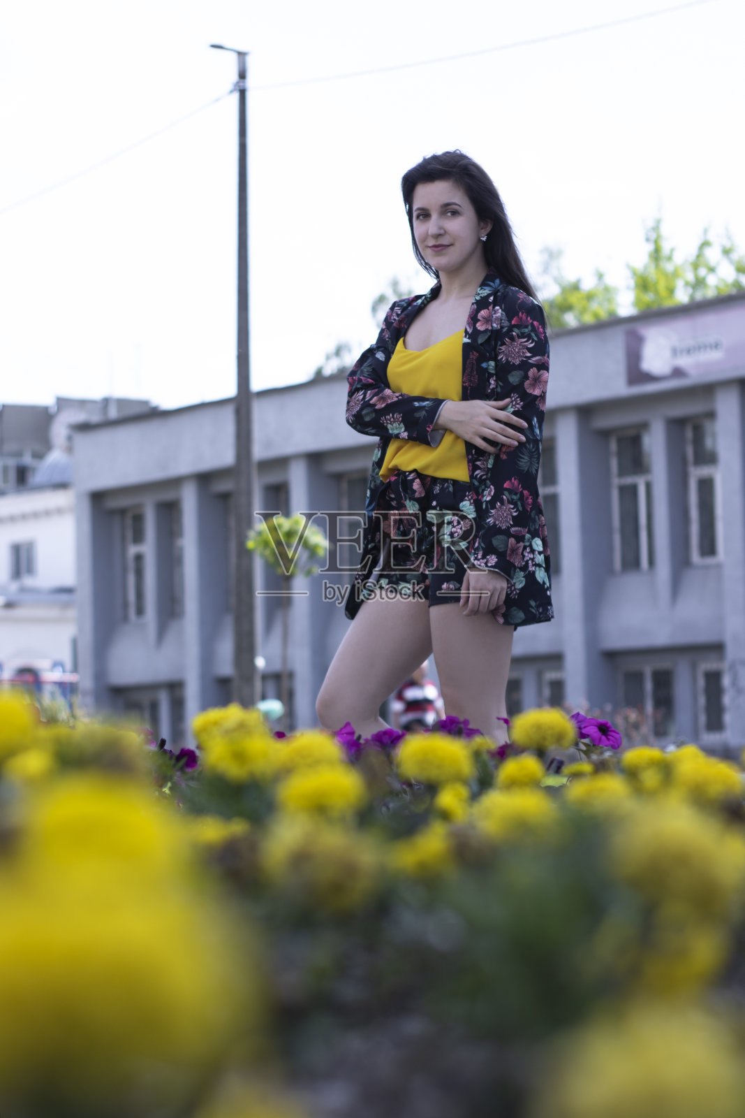 迷人的年轻女子在黄色t恤和花短裤服装。在一丛花丛附近。副本的空间。照片摄影图片