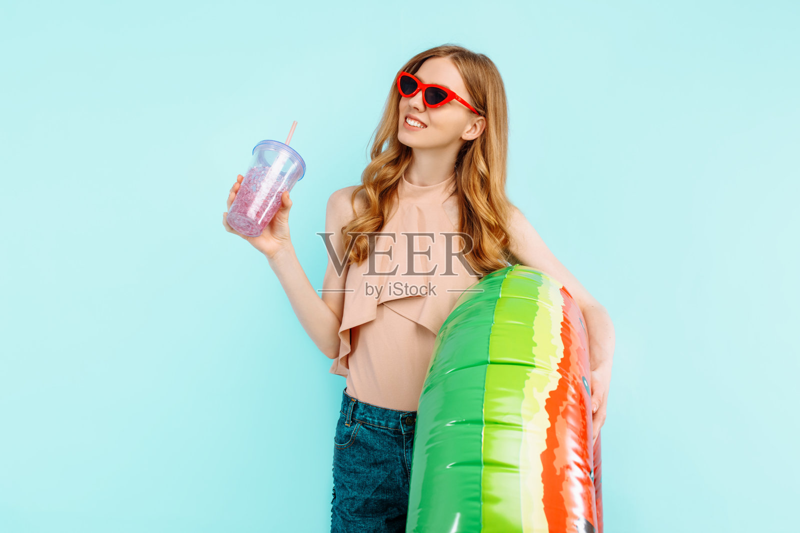 快乐的女孩穿着泳衣，戴着太阳镜，拿着一杯鸡尾酒和一个蓝色背景的充气游泳圈照片摄影图片