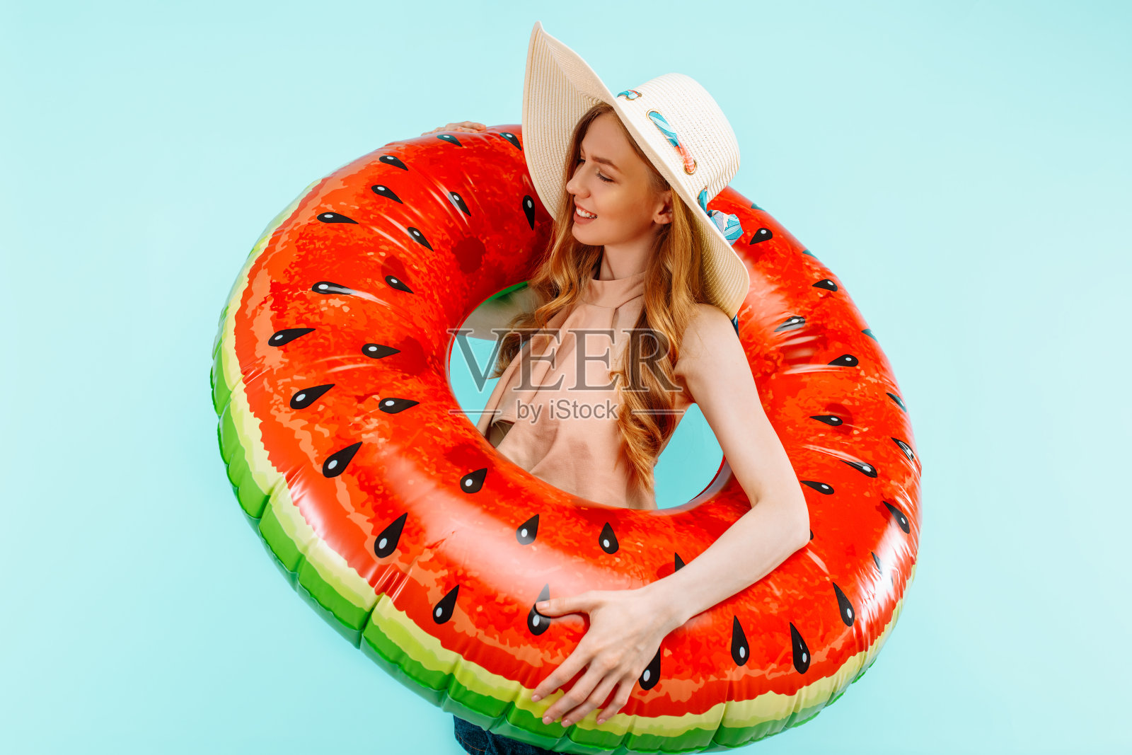 迷人的快乐的女孩戴着一顶夏天的帽子，在蓝色的背景上拿着一个充气的游泳圈照片摄影图片