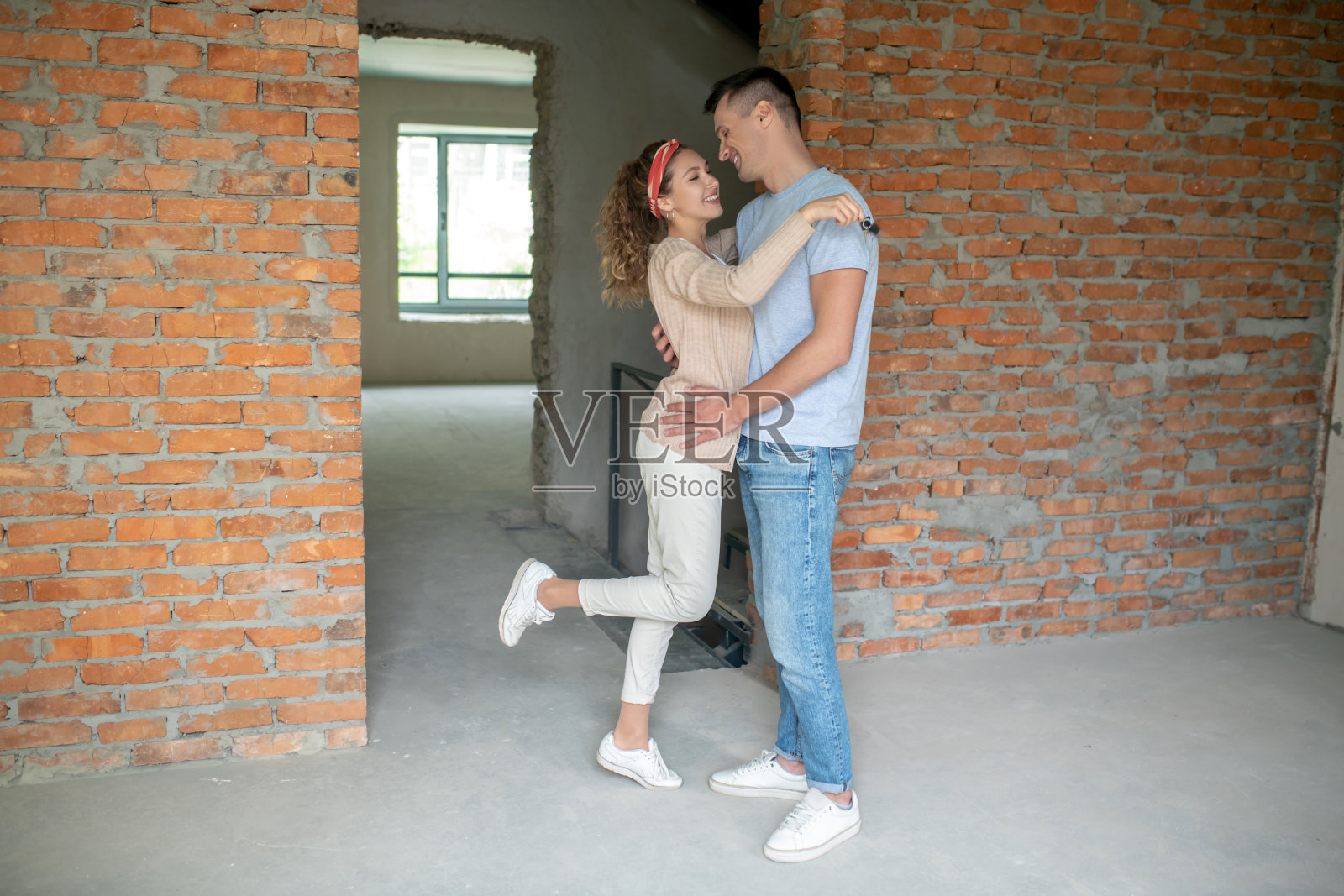 一对年轻夫妇站在有砖墙的空房间里拥抱着照片摄影图片