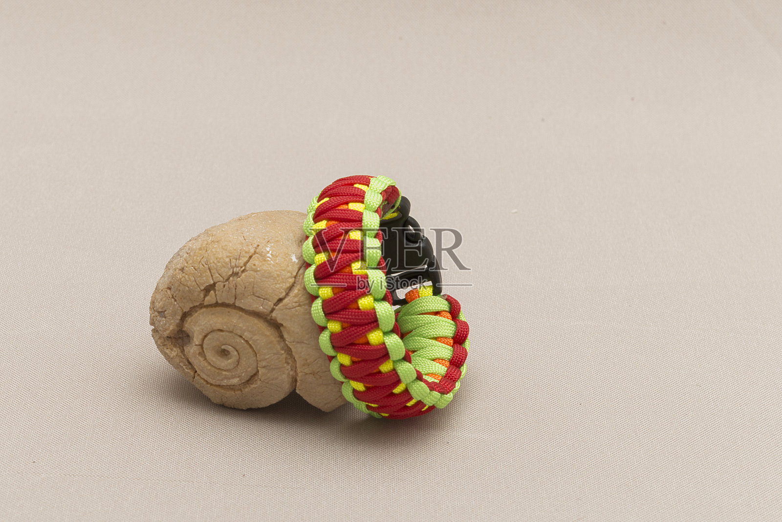彩色伞绳手镯，放置在化石贝壳附近，孤立在浅棕色的背景上照片摄影图片