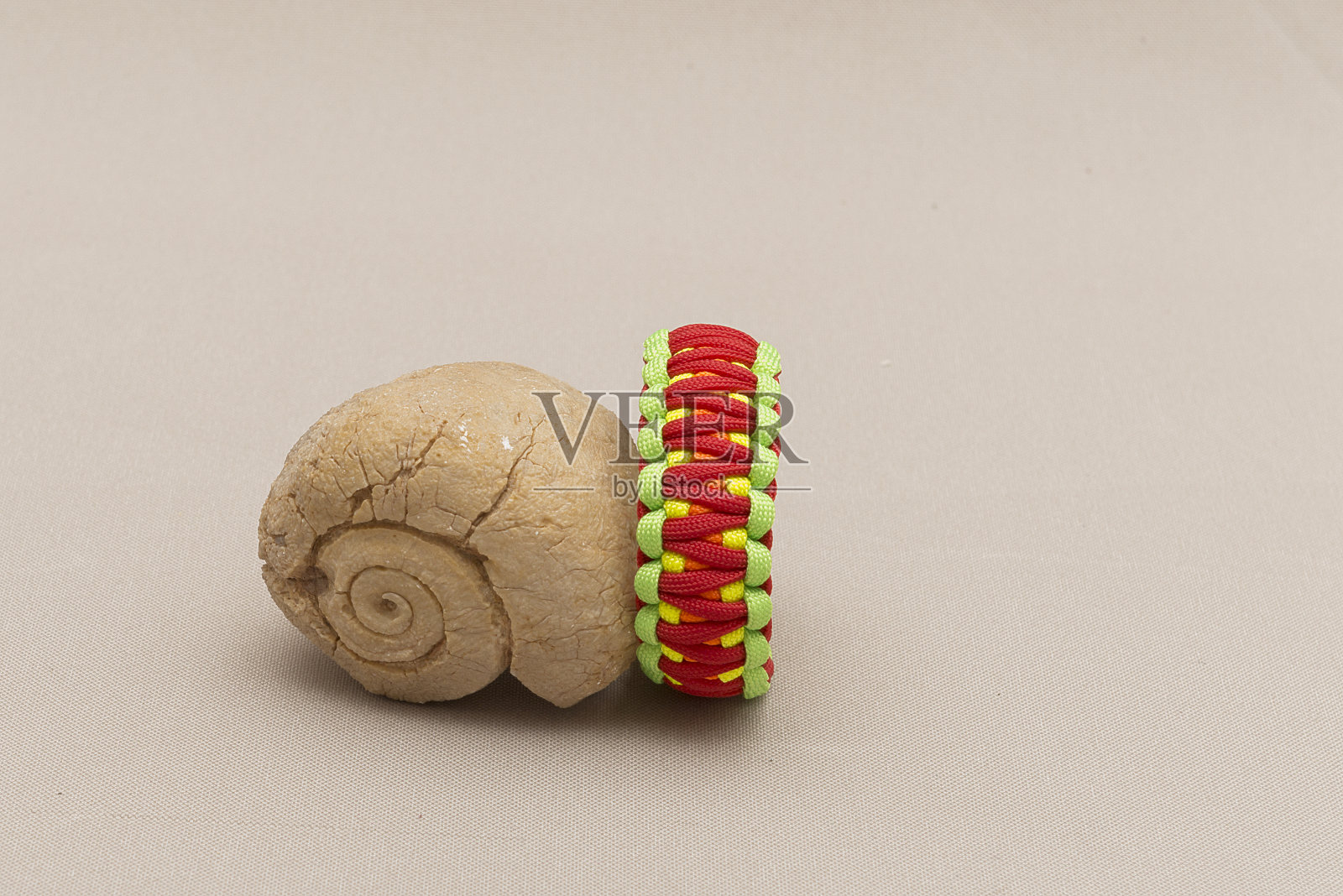 彩色伞绳手镯，放置在化石贝壳附近，孤立在浅棕色的背景上照片摄影图片