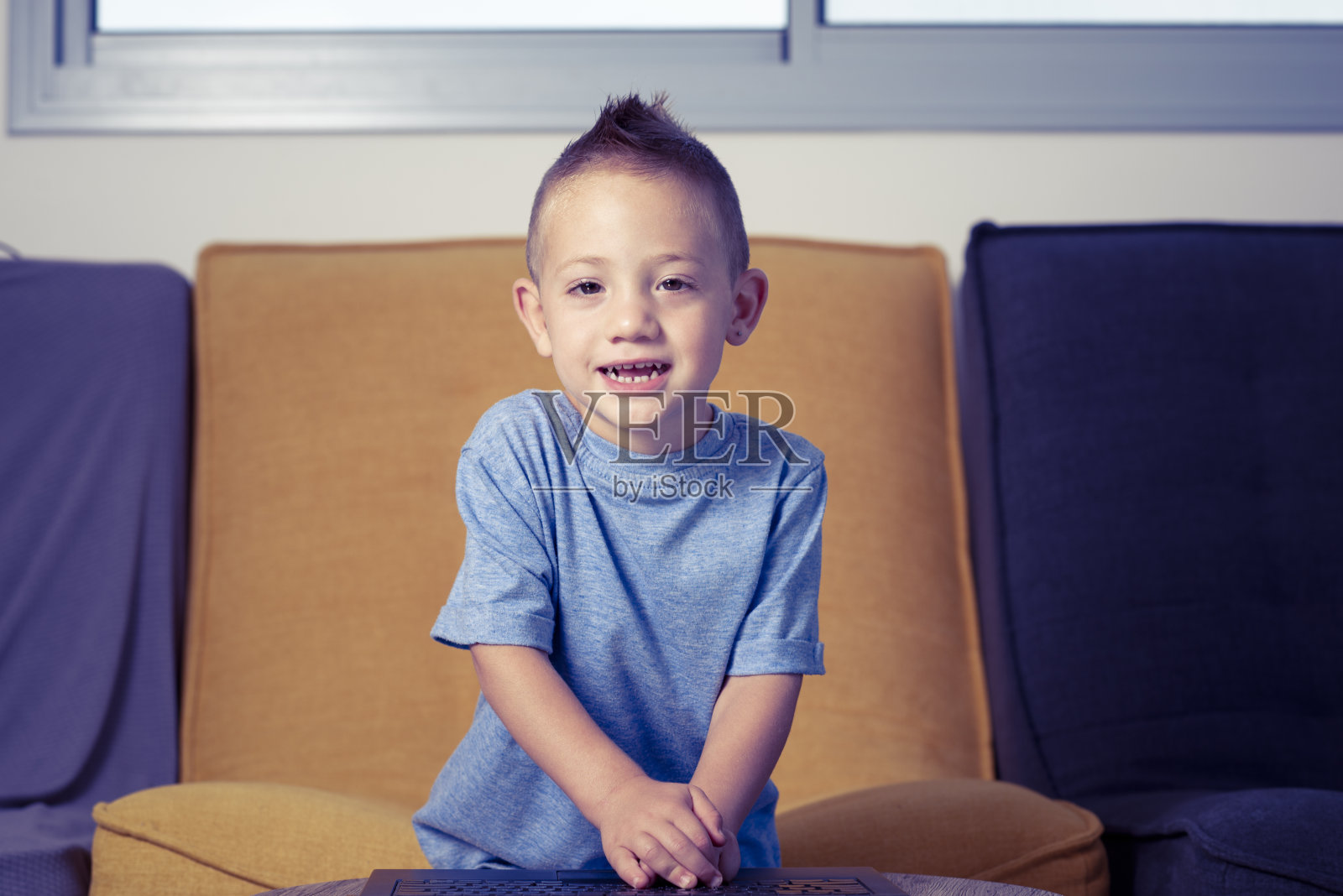 坐在家里，在笔记本电脑键盘上打字的小男孩照片摄影图片