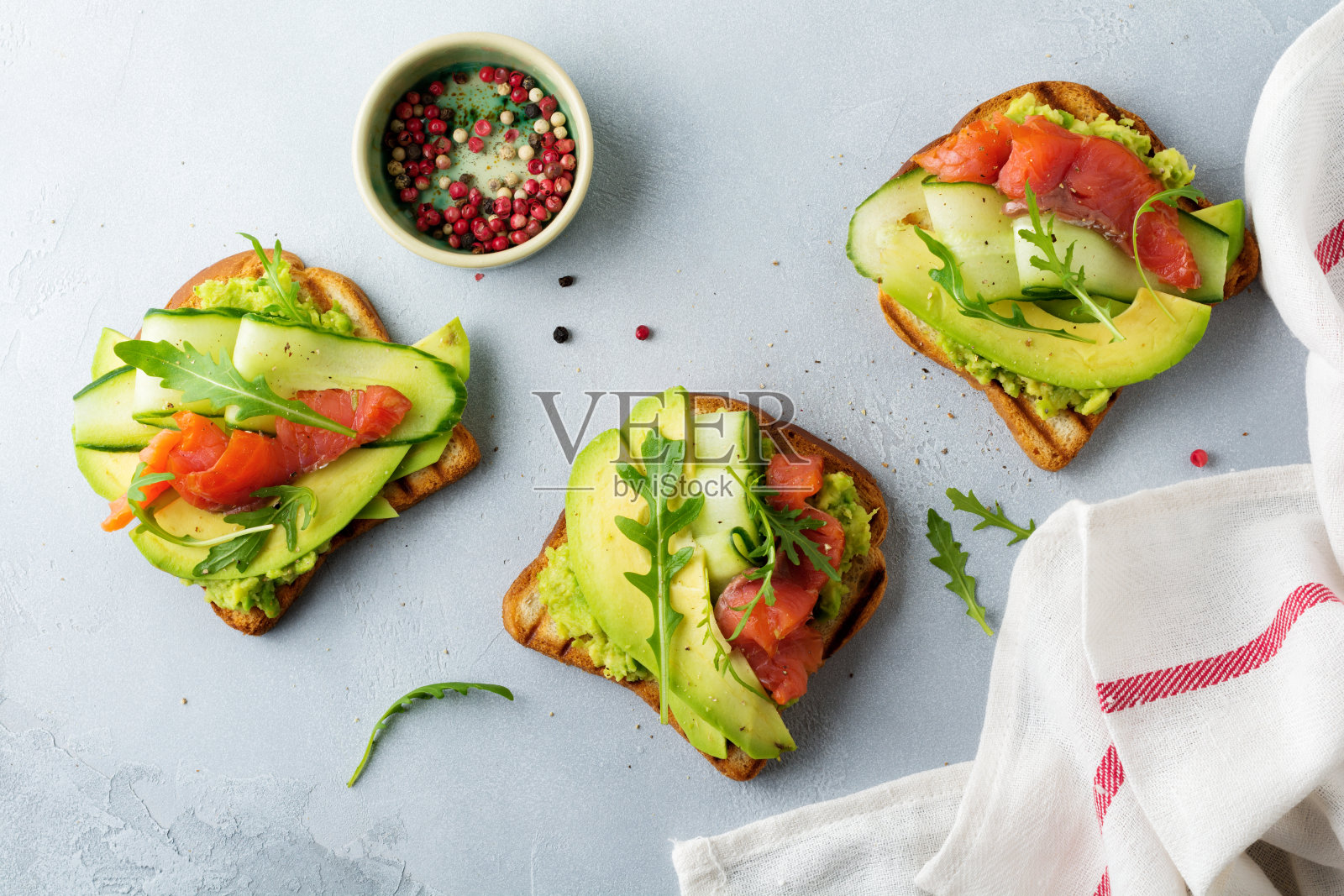 灰色混凝土背景下的木架上，烤着鳟鱼、鲑鱼、鳄梨、黄瓜和芝麻菜。有选择性的重点。前视图。本空间照片摄影图片