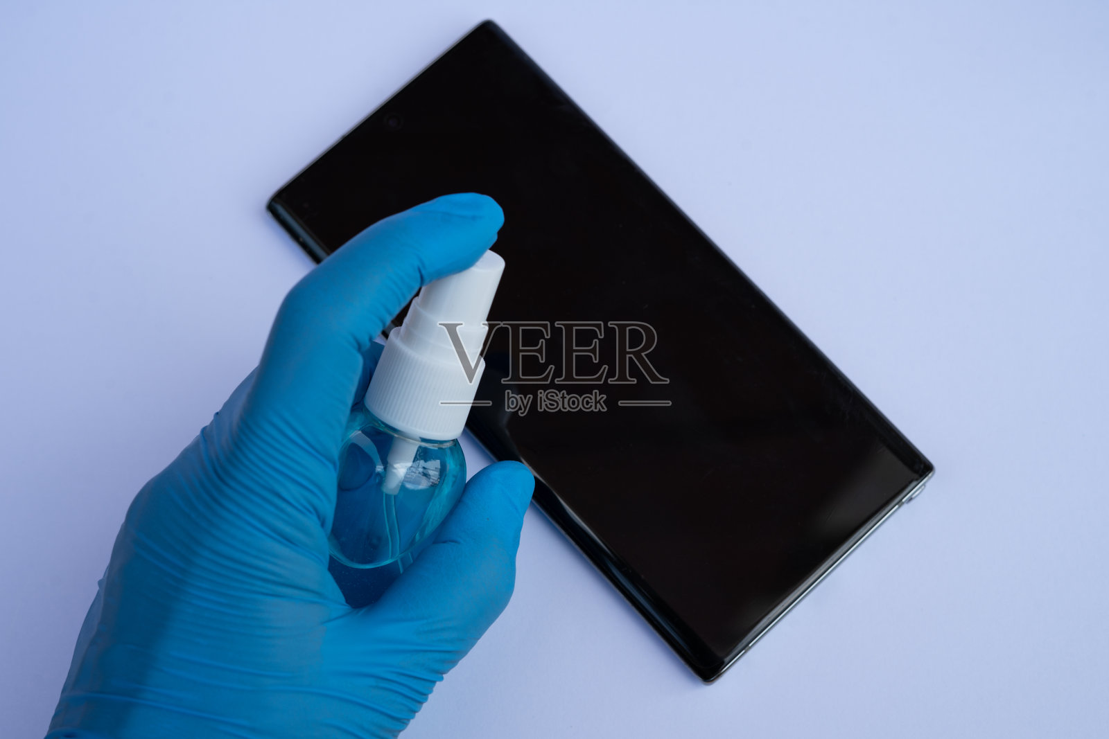 手用酒精消毒液喷向智能手机，防止细菌和病毒的传播。抗冠状病毒，新冠肺炎概念。照片摄影图片