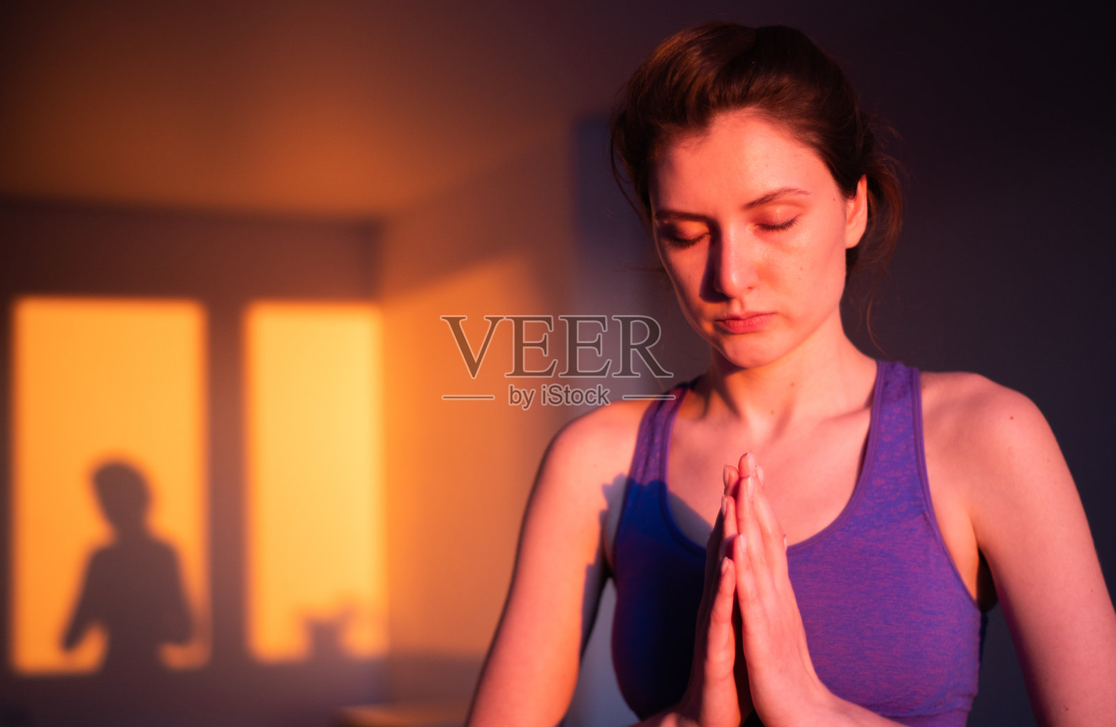 日落时分，一位平静的年轻女子在客厅里沉思。瑜伽和禅宗概念，呼吸练习为健康的生活方式照片摄影图片
