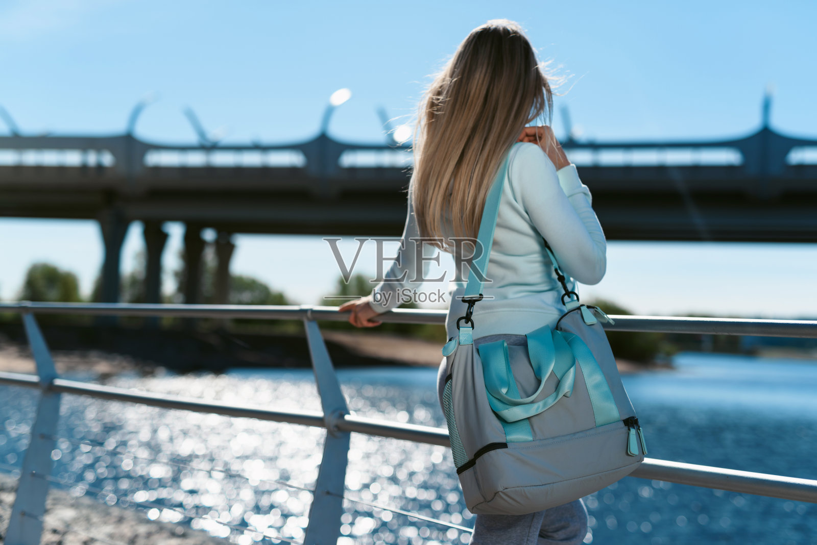 一个年轻女子，带着运动包，穿着运动服，走在人行道上，听着音乐，准备街头运动。照片摄影图片