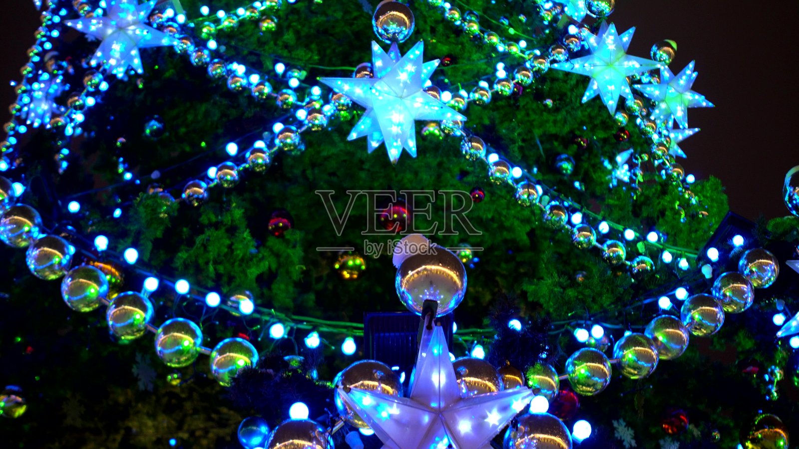 近距离的圣诞树在广场上装饰着五颜六色的花环，球和星星照片摄影图片