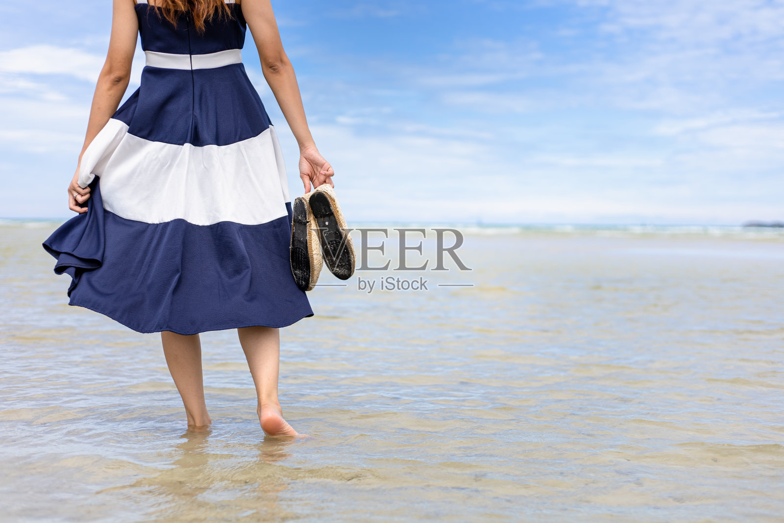 女人光着脚走在夏天沿着海浪和沙滩上的海水和沙子。照片摄影图片