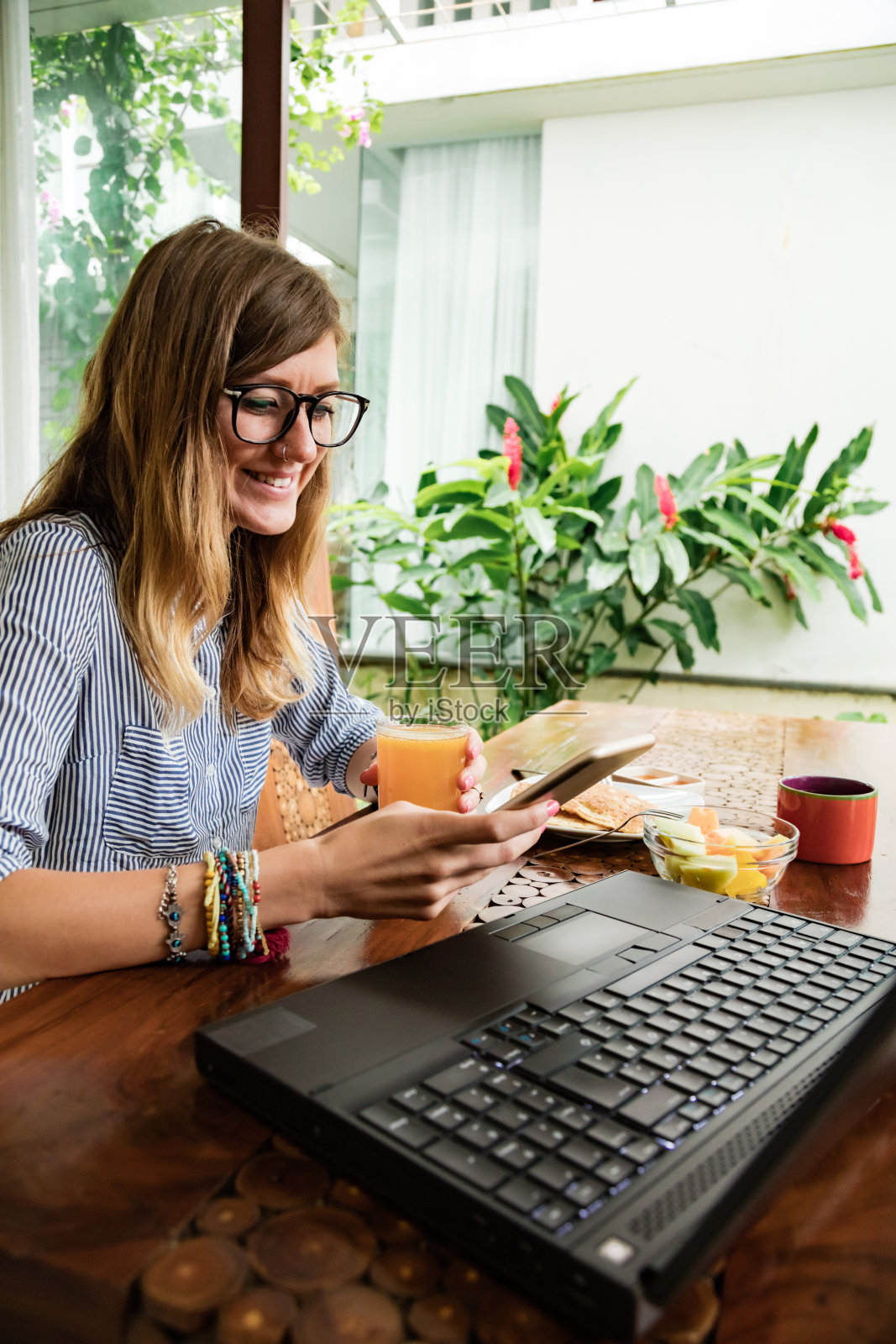 妇女使用笔记本电脑和手机在家里吃早餐-自由职业者的概念。照片摄影图片