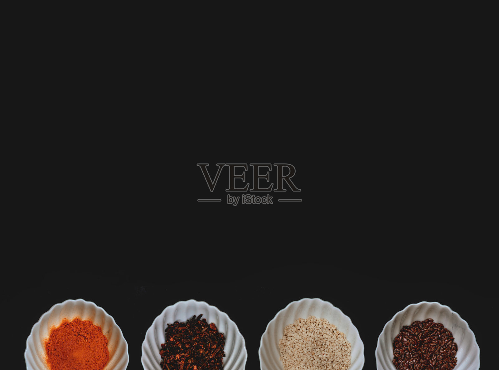 在孤立的黑色背景上，白色杯子里的香料和谷物的边缘。照片摄影图片