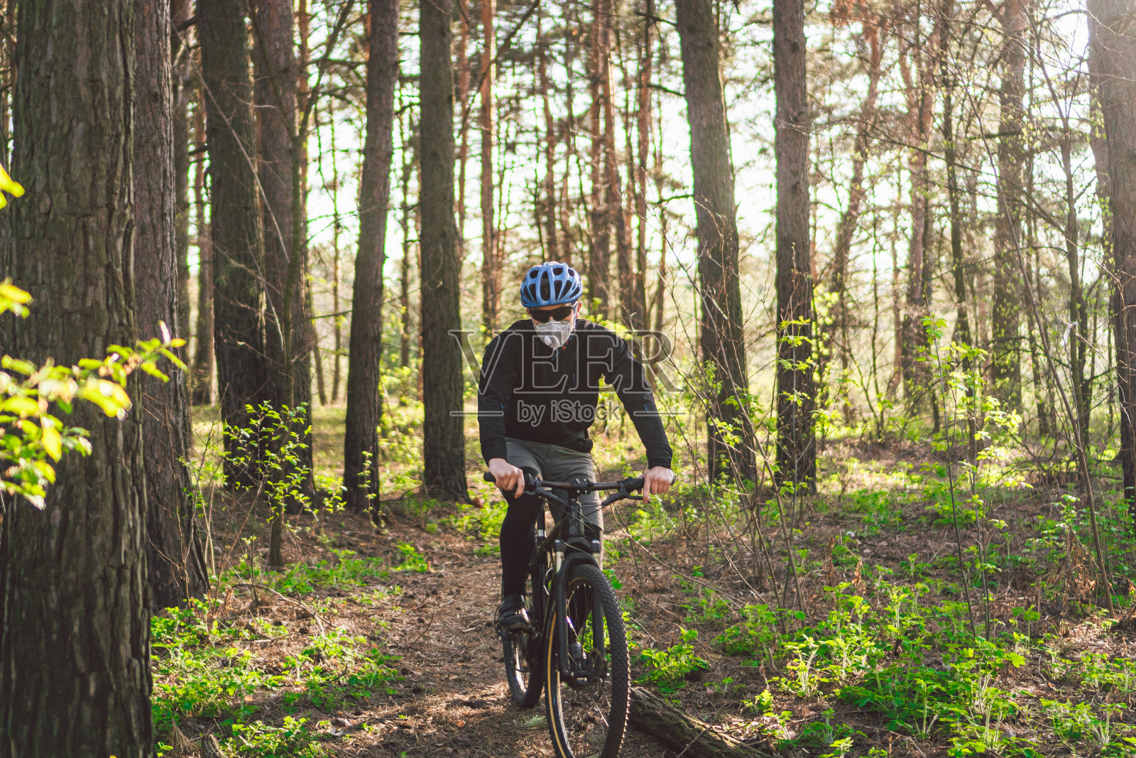 骑自行车的人戴着防污染口罩。年轻小伙子戴着pm2.5过滤器的呼吸器，在公园里骑自行车。Covid - 19隔离运动。山地自行车手在森林里骑自行车。登山运动员在一条小路上照片摄影图片