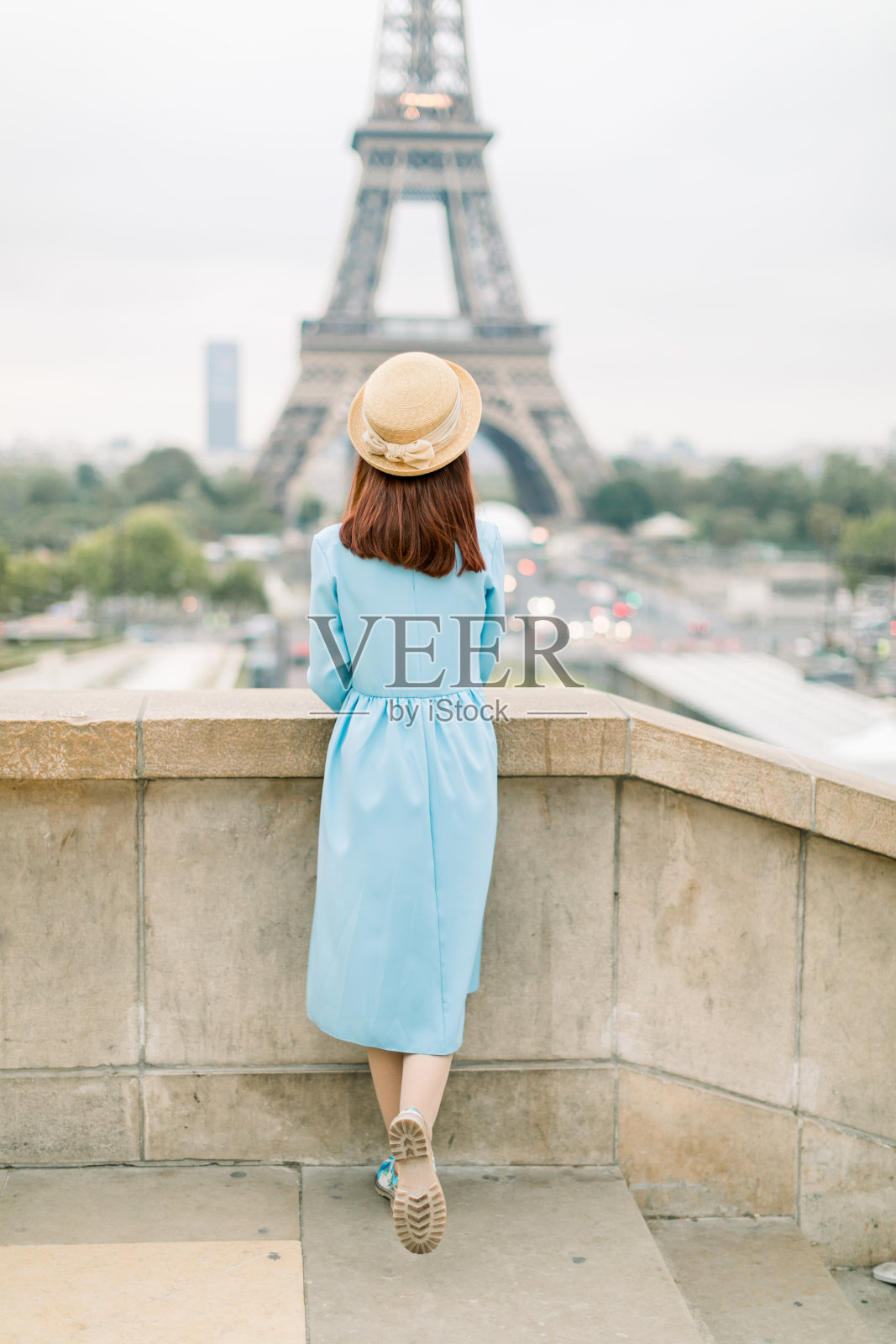 背影肖像年轻迷人的女人在帽子，蓝色的衣服，看着巴黎的埃菲尔铁塔。年轻时髦的女人欣赏着埃菲尔铁塔上的美景。旅行,旅游的概念照片摄影图片