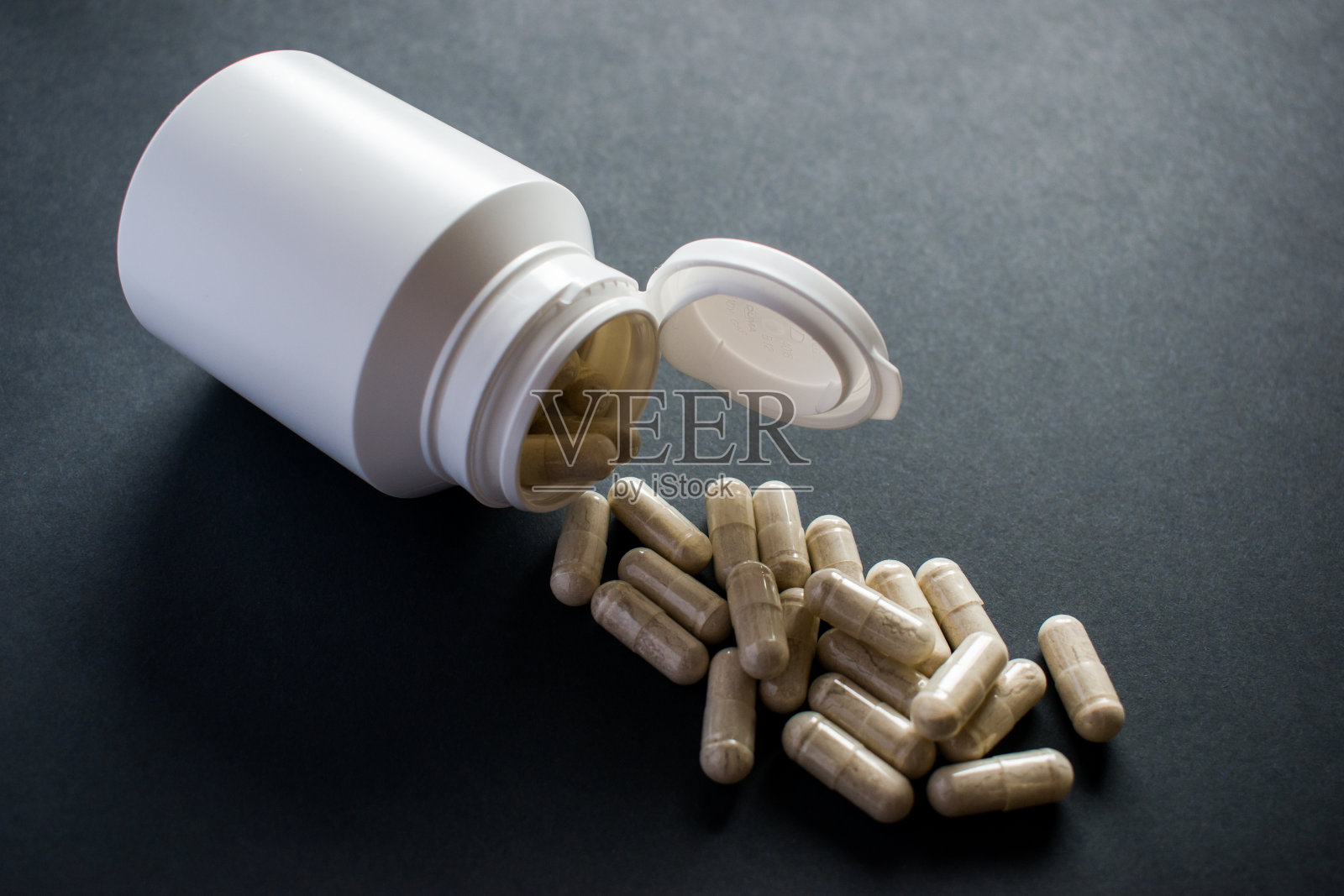 在黑色背景上，医药药丸从药瓶中溢出照片摄影图片