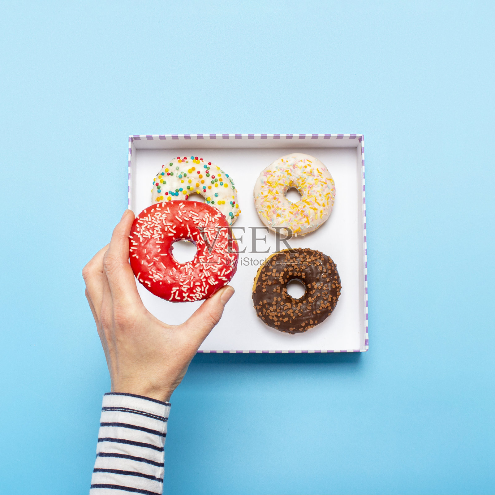 在蓝色背景下，女性的手拿着一个甜甜圈。概念糖果店，糕点店，咖啡店。横幅。平躺，俯视图照片摄影图片