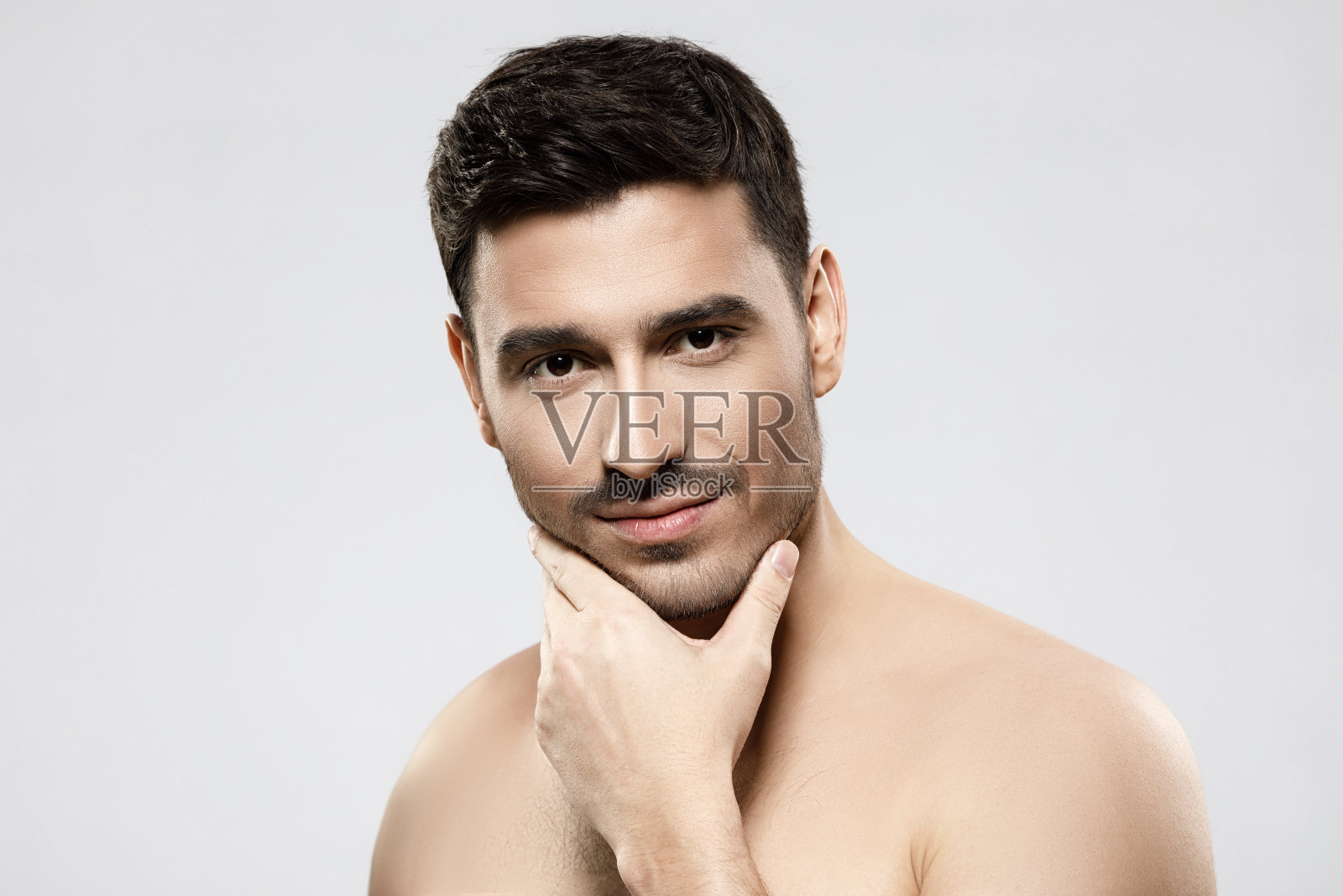 肖像的年轻英俊的男子没有穿衬衫，触摸他的下巴沉思的脸。男性美容护肤理念，孤立于灰色背景之上照片摄影图片
