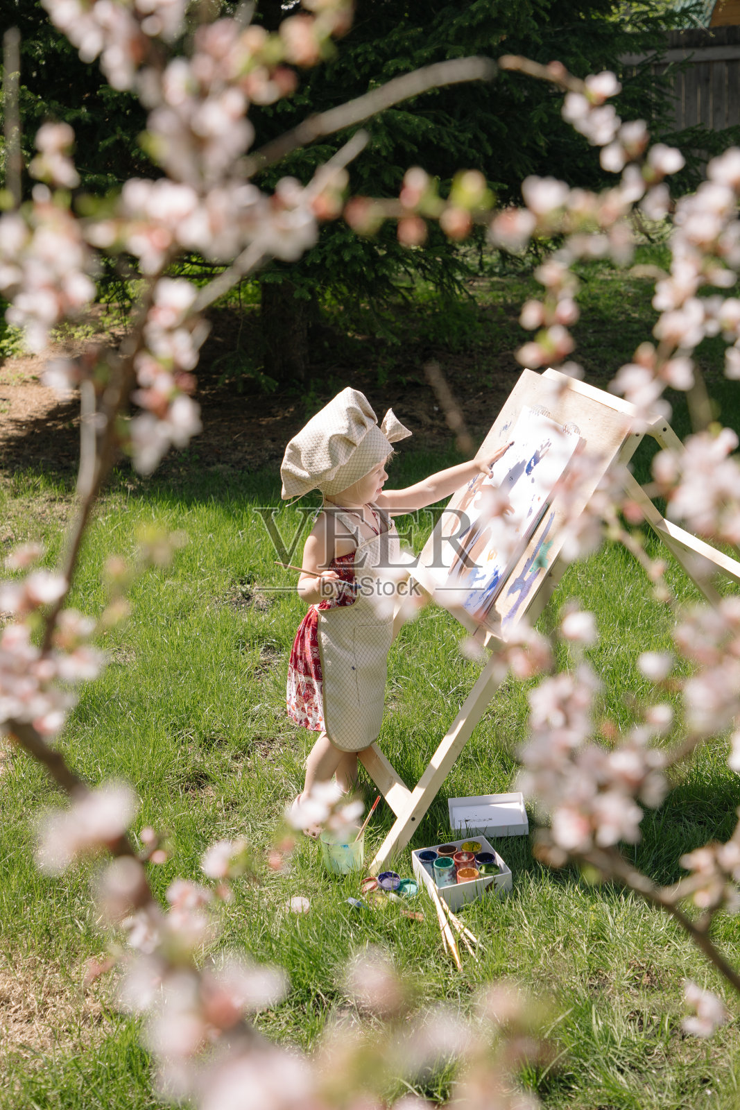 大自然中的小女孩在画架上画着盛开的樱桃照片摄影图片