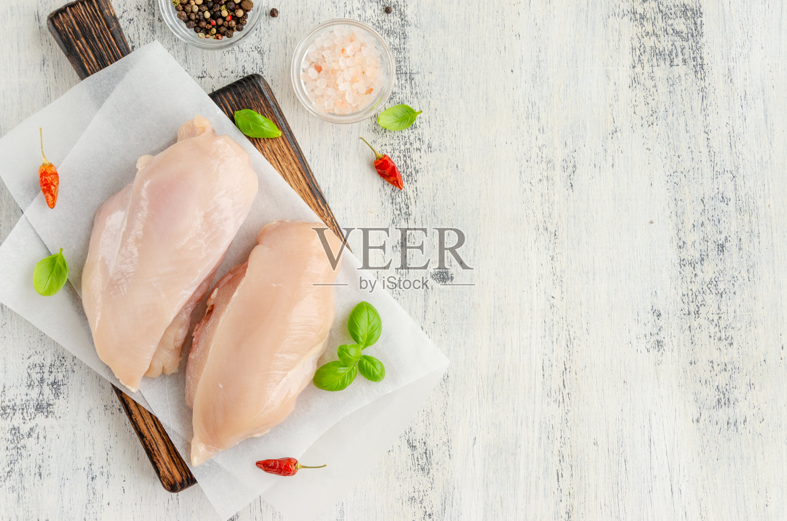 生鸡胸肉放在砧板上，配上罗勒和其他香料，以浅色的木头为背景。健康食品。水平,复制空间。照片摄影图片