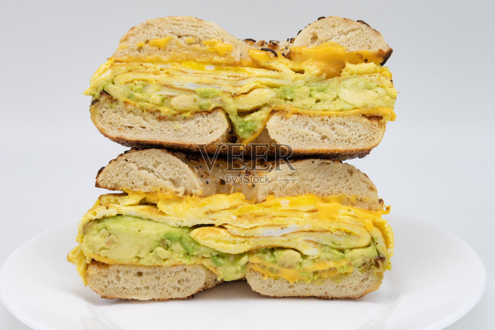 白盘子里的百吉饼，牛油果蛋和奶酪，切成两半照片摄影图片