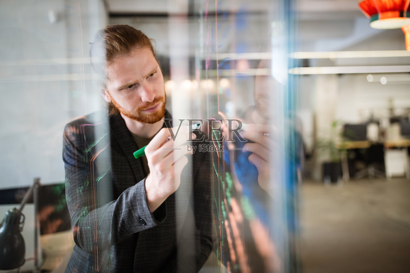 英俊的男人在办公室的玻璃板上工作和写作。商业、技术、研究理念照片摄影图片