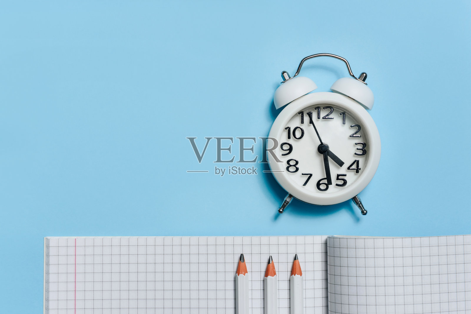平铺排版，一个闹钟，一个打开的笔记本和蓝色背景的铅笔照片摄影图片