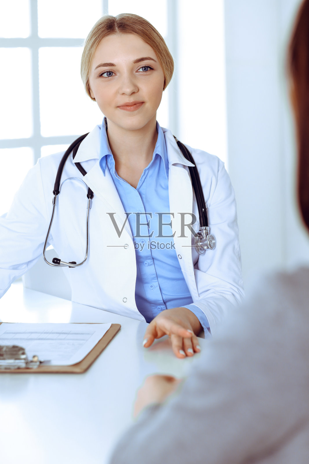 年轻女医生和病人在医院办公室进行体检。蓝色的治疗师衬衫看起来不错。医疗保健理念照片摄影图片