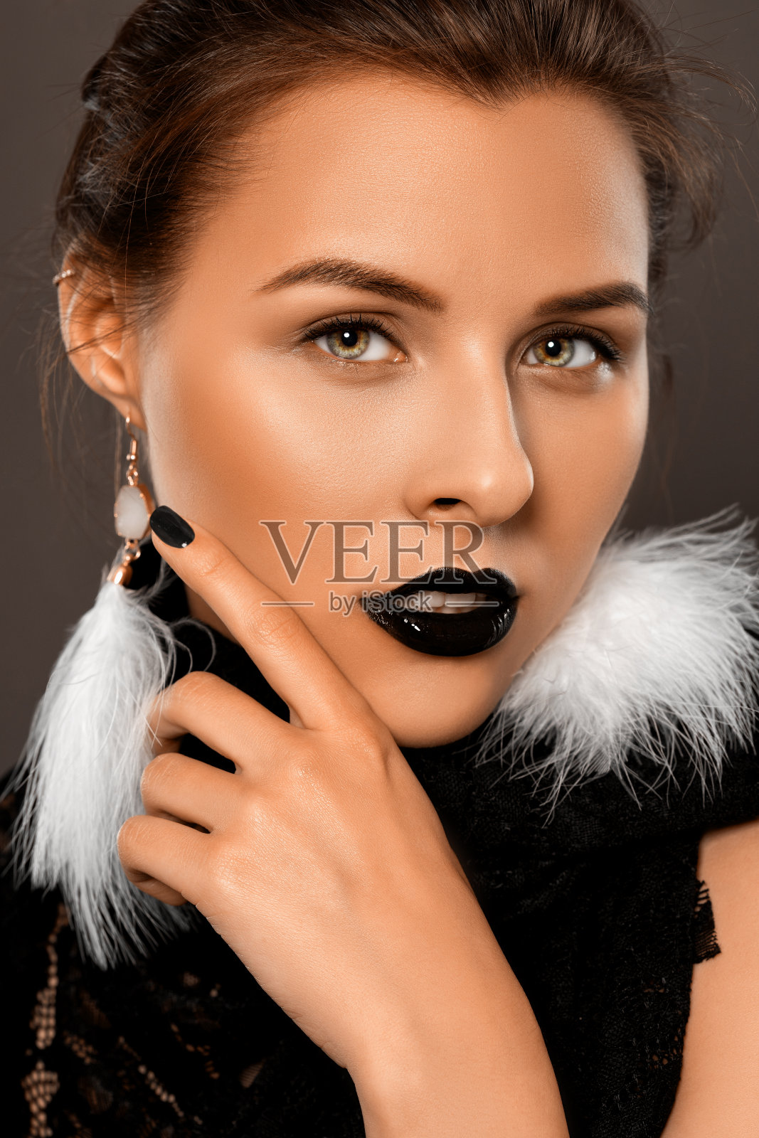 女人用美丽的妆容和黑色的口红在她的嘴唇，哥特式风格。她戴着白色羽毛耳环。化妆和美容的概念。照片摄影图片