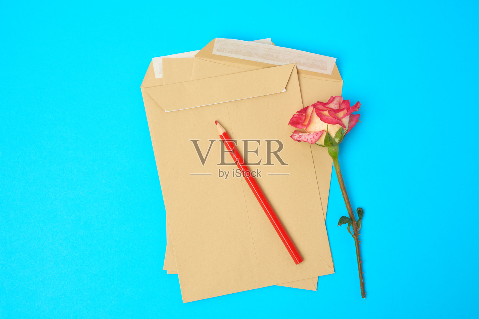 红色盛开的玫瑰和棕色的纸信封在蓝色的背景照片摄影图片