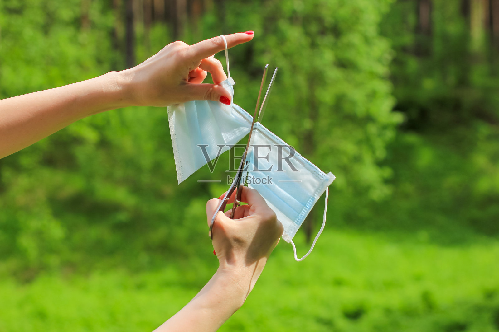 结束covid-19、大流行、危机和封锁的概念。一名年轻女子手中的剪刀正在剪一个医用呼吸面罩。回到正常生活。照片摄影图片