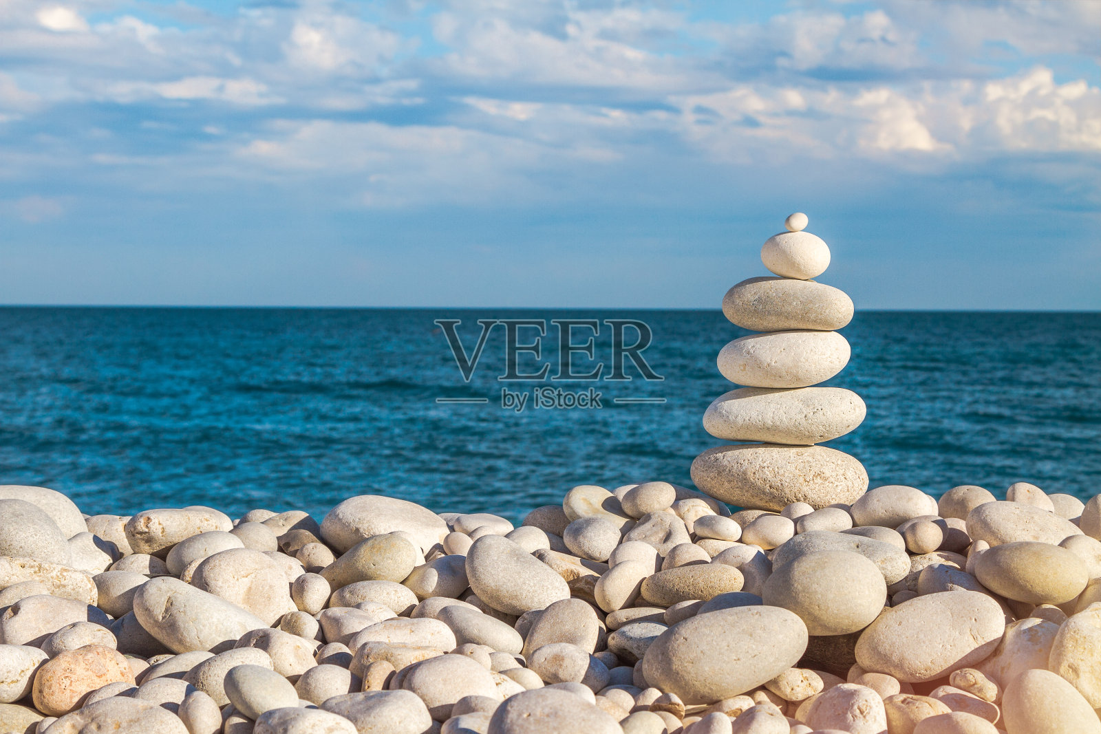 石堆禅宗金字塔的白色卵石上的石头海滩在一个蓝色的海和云的天空的背景。照片摄影图片