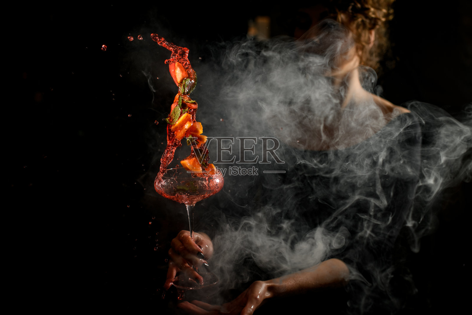 在黑暗的酒吧里，一个女人拿着一个洒着酒精鸡尾酒的杯子照片摄影图片