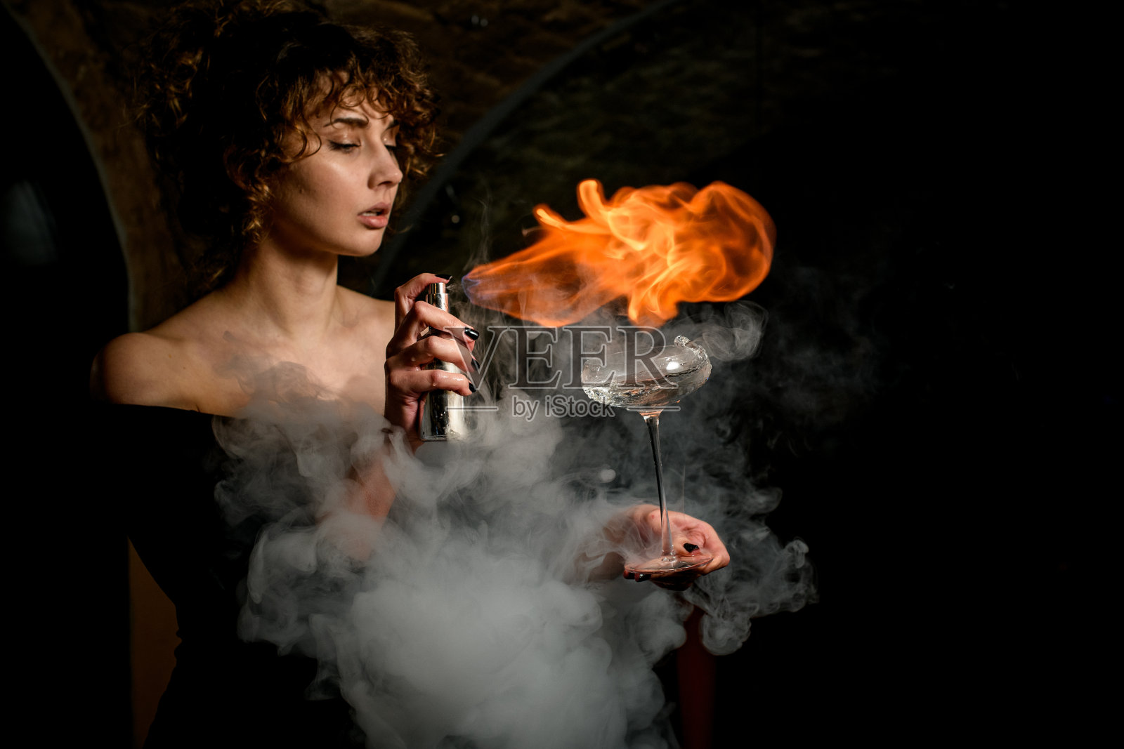 美丽的女人拿着杯子，洒着饮料，然后在上面生火。照片摄影图片