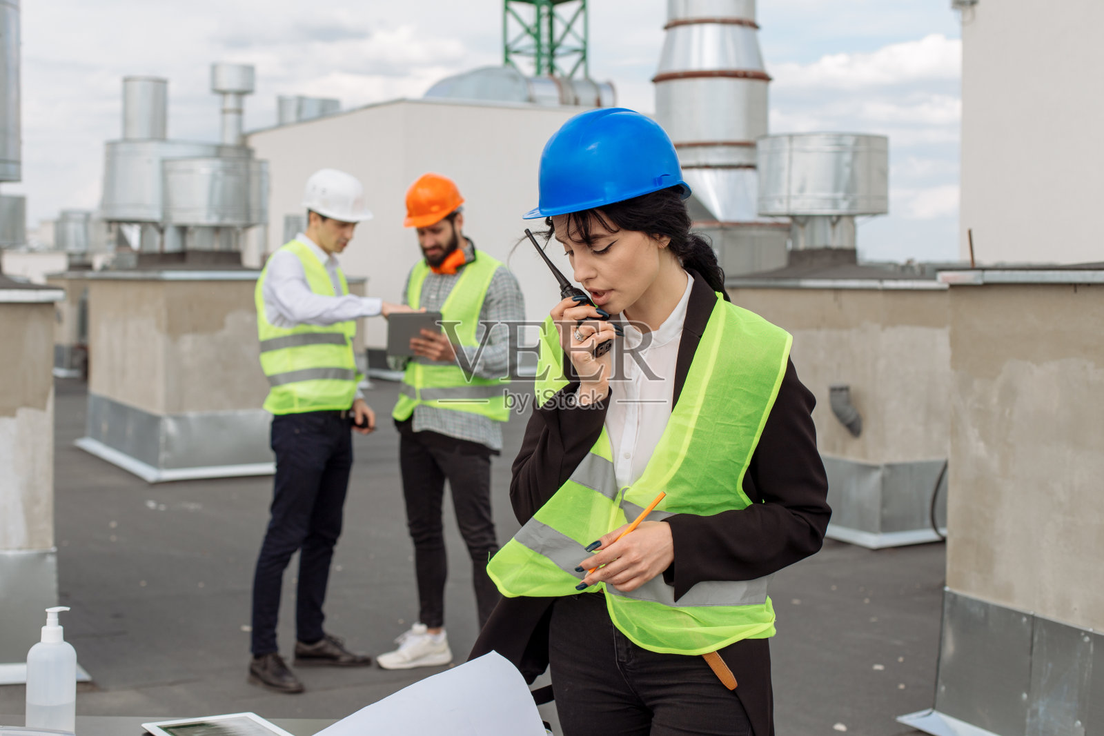 在建筑工地的屋顶上，美丽的工程师与一些使用定额的工人交谈照片摄影图片