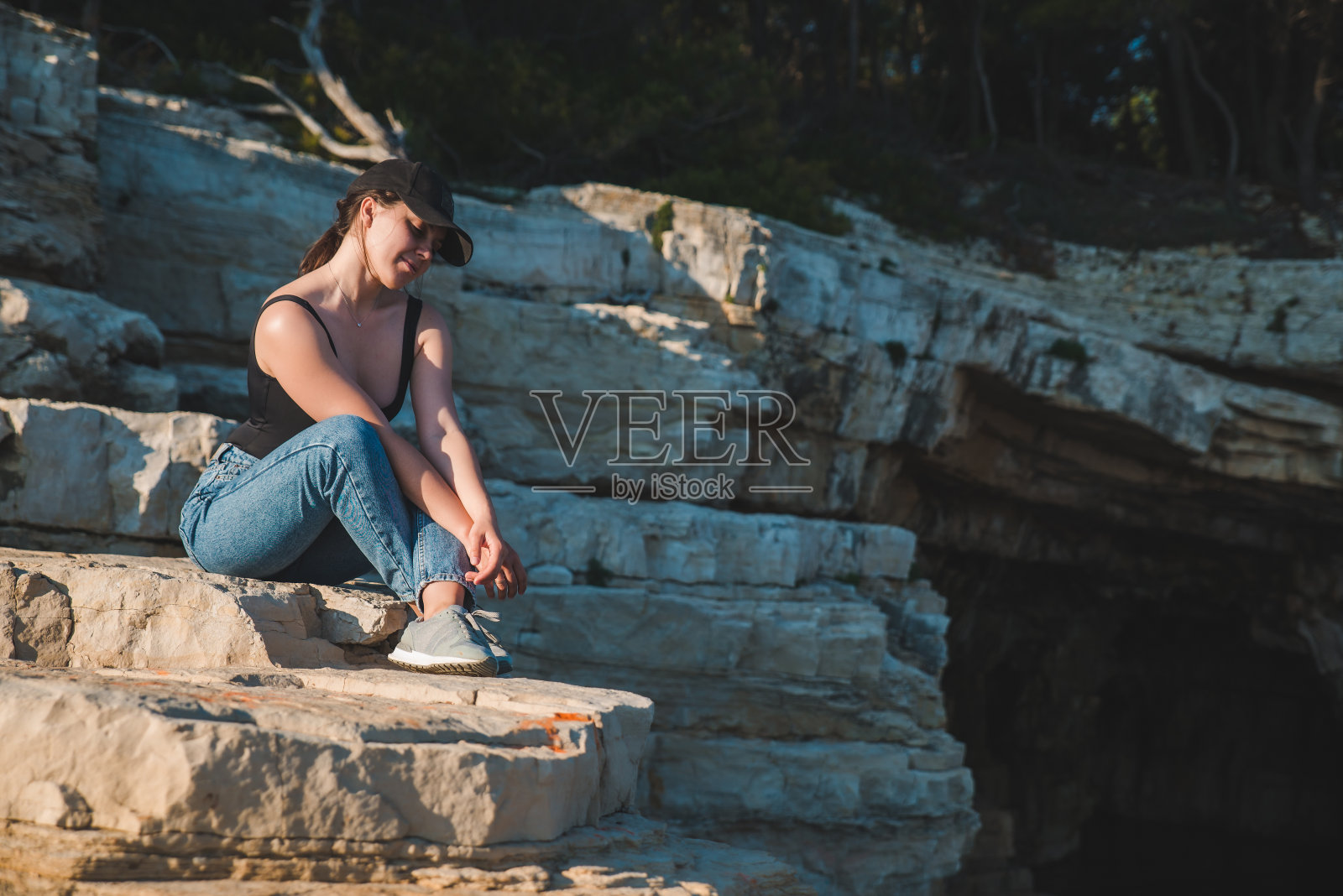 年轻漂亮的女人坐在悬崖上看着大海照片摄影图片