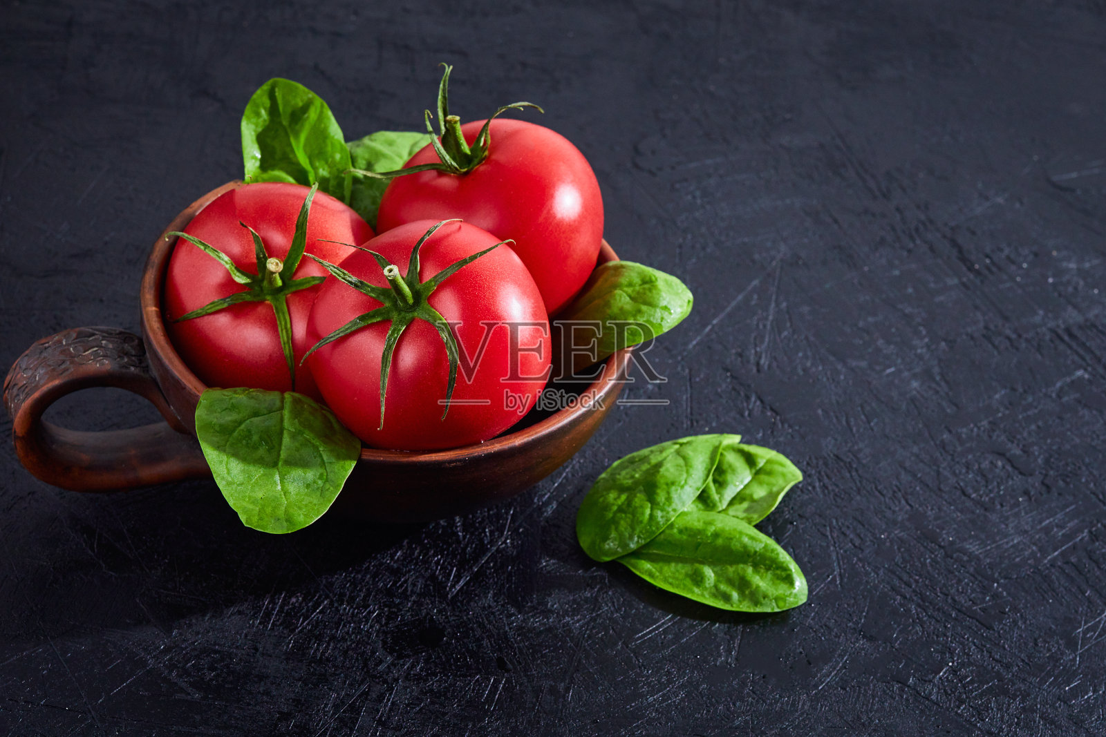 新鲜的葡萄西红柿与菠菜叶在黑色的石头背景。素食主义者的饮食。草、烹饪概念。照片摄影图片