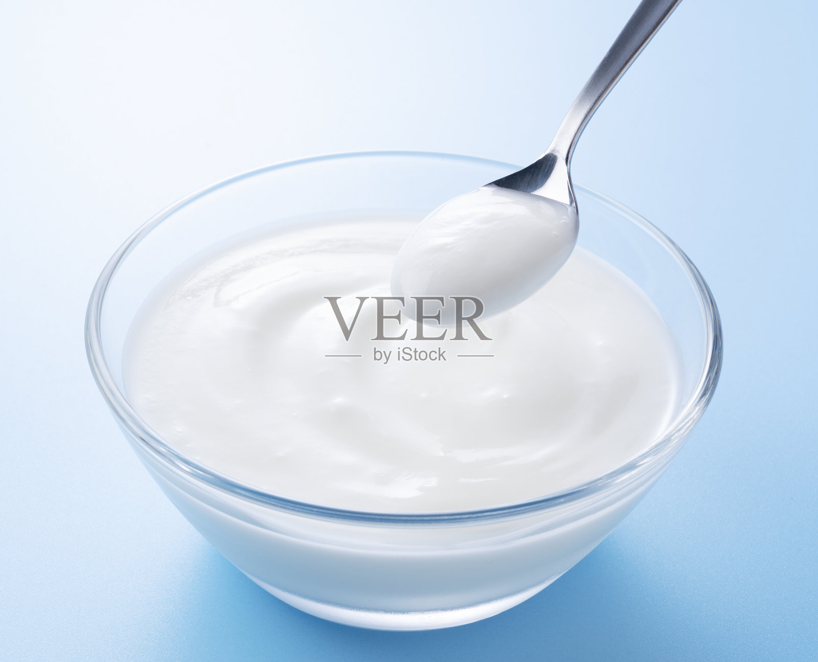 酸奶在一个玻璃碗和一勺酸奶。照片摄影图片