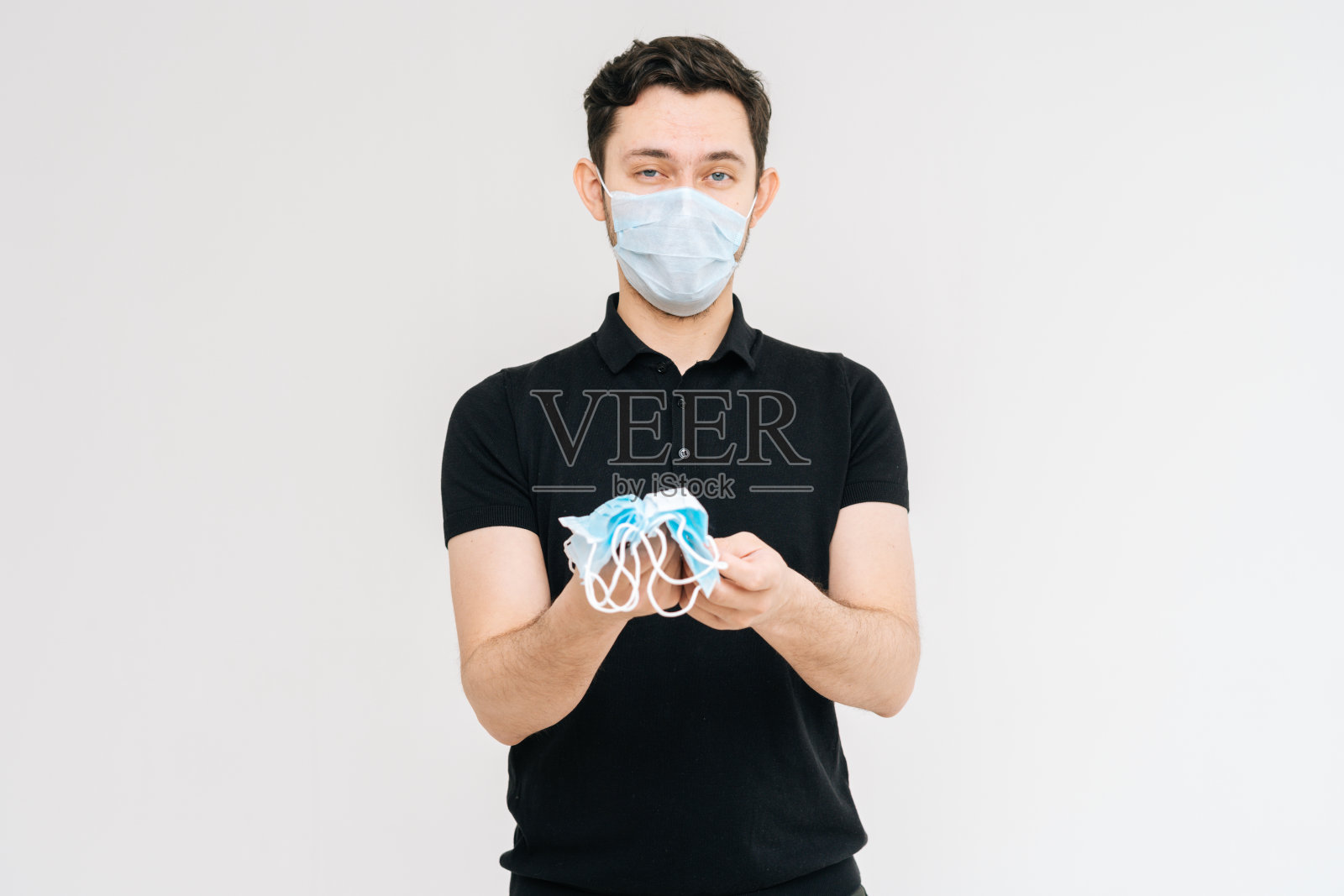 摄影棚拍摄了一名戴着防护口罩的年轻人，手里拿着很多医用口罩。照片摄影图片