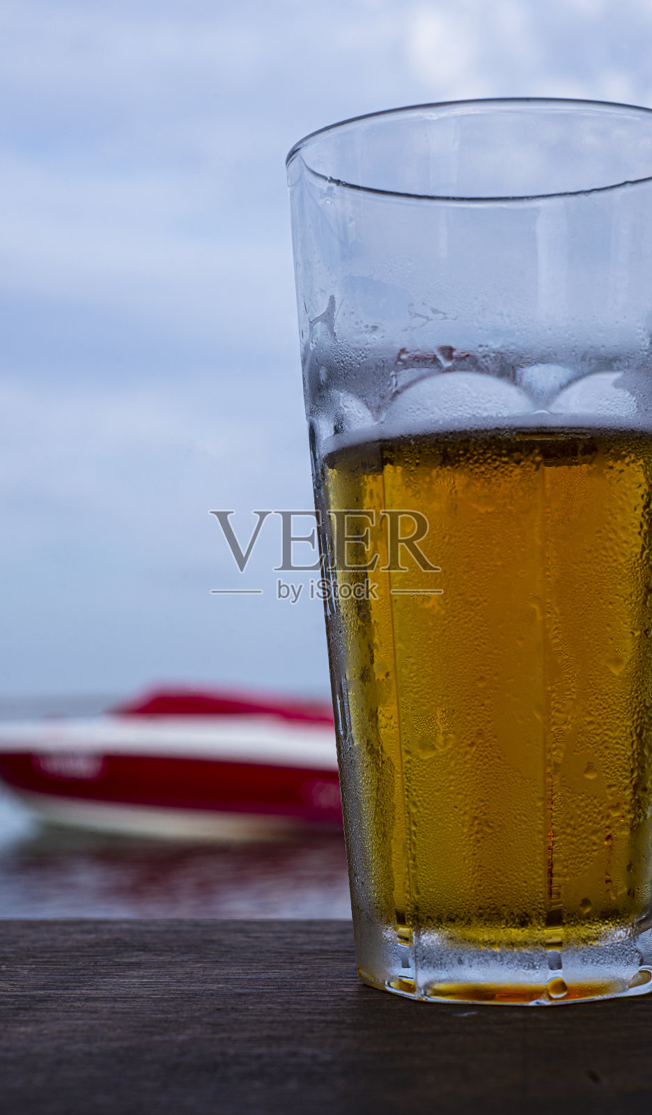 在水和小船的背景下，在海滩上喝着金色啤酒。照片摄影图片