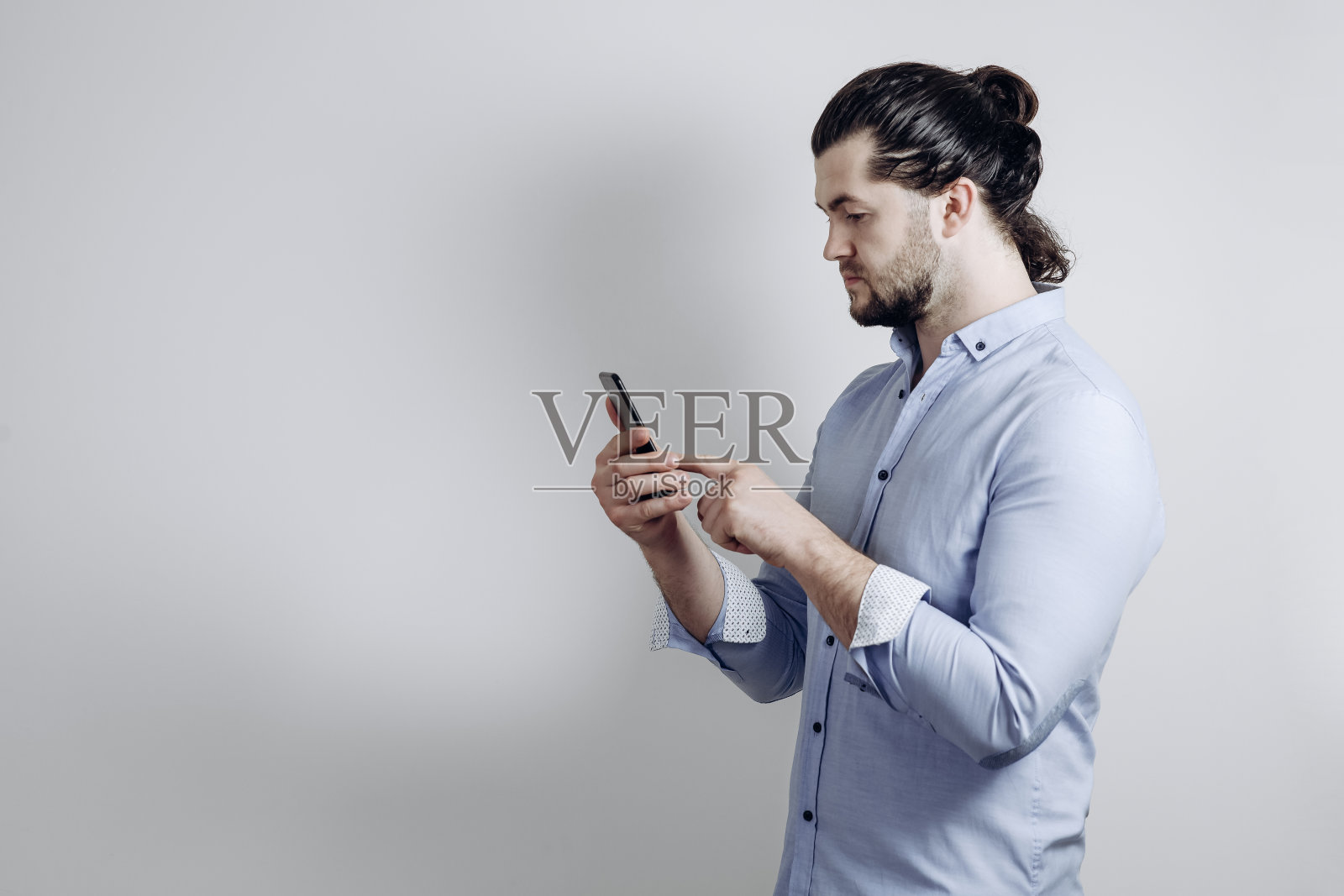 一个穿衬衫、留长发的男人在回复短信。灰色背景照片摄影图片